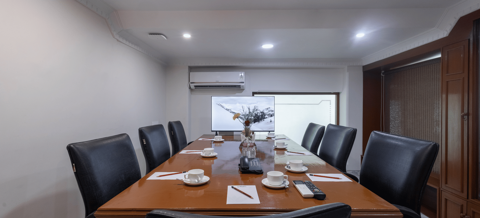 A private meeting room with a large wooden table, set for a meeting with black leather high-backed chairs at Pravasa Stay, Vadodara.