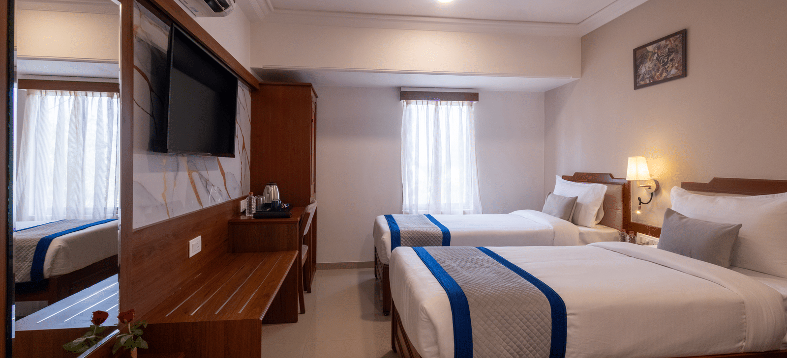 View of the twin-bedded hotel room, reflected partially in the large, dark wooden mirror over the desk/console at Pravasa Stay, Vadodara.