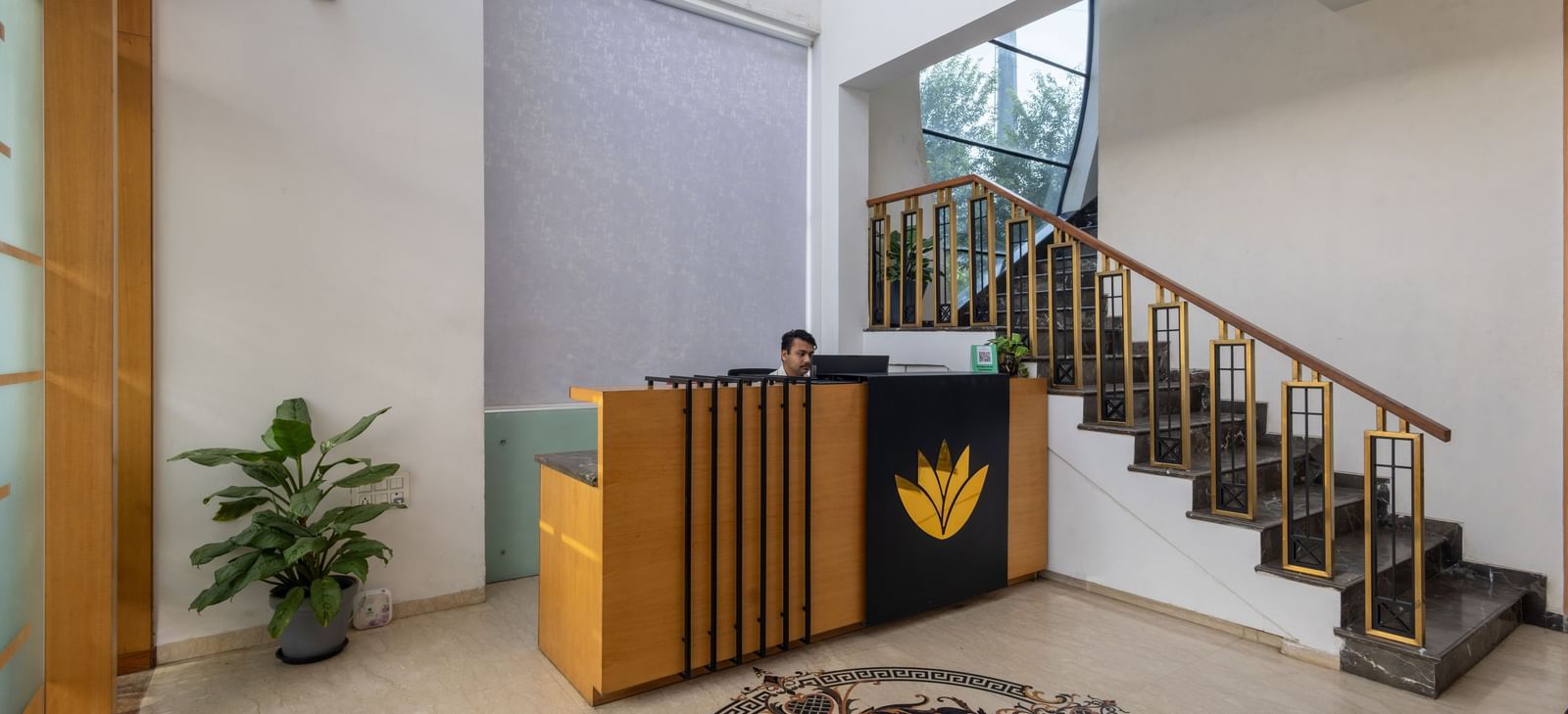 Lobby and reception desk of Pravasa Stay Vijay Nagar, Indore, showcasing a desk, a flight of stairs leading to the floor above, and a floor with patterned tiles in the centre.