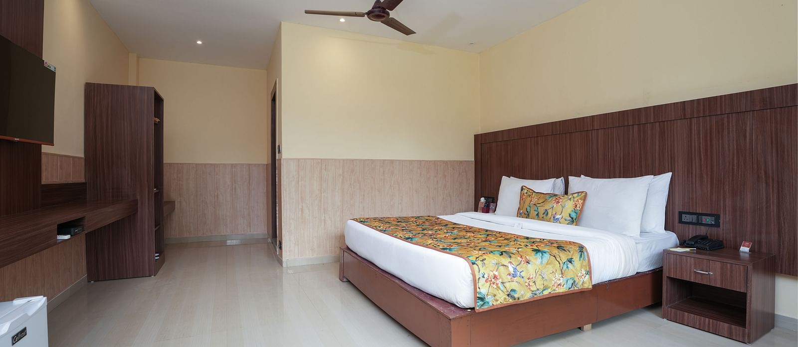 Premium Room with a large bed, wooden furniture and storage, mini fridge, and wall-mounted TV at Summit Green Lake Tea Resort & Spa, Kaziranga