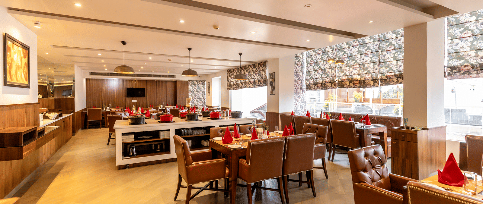 A restaurant with multiple tables, chairs, buffet counters, and lighting fixtures arranged indoors at Indraprastha Resort & Spa, McLeod Ganj.