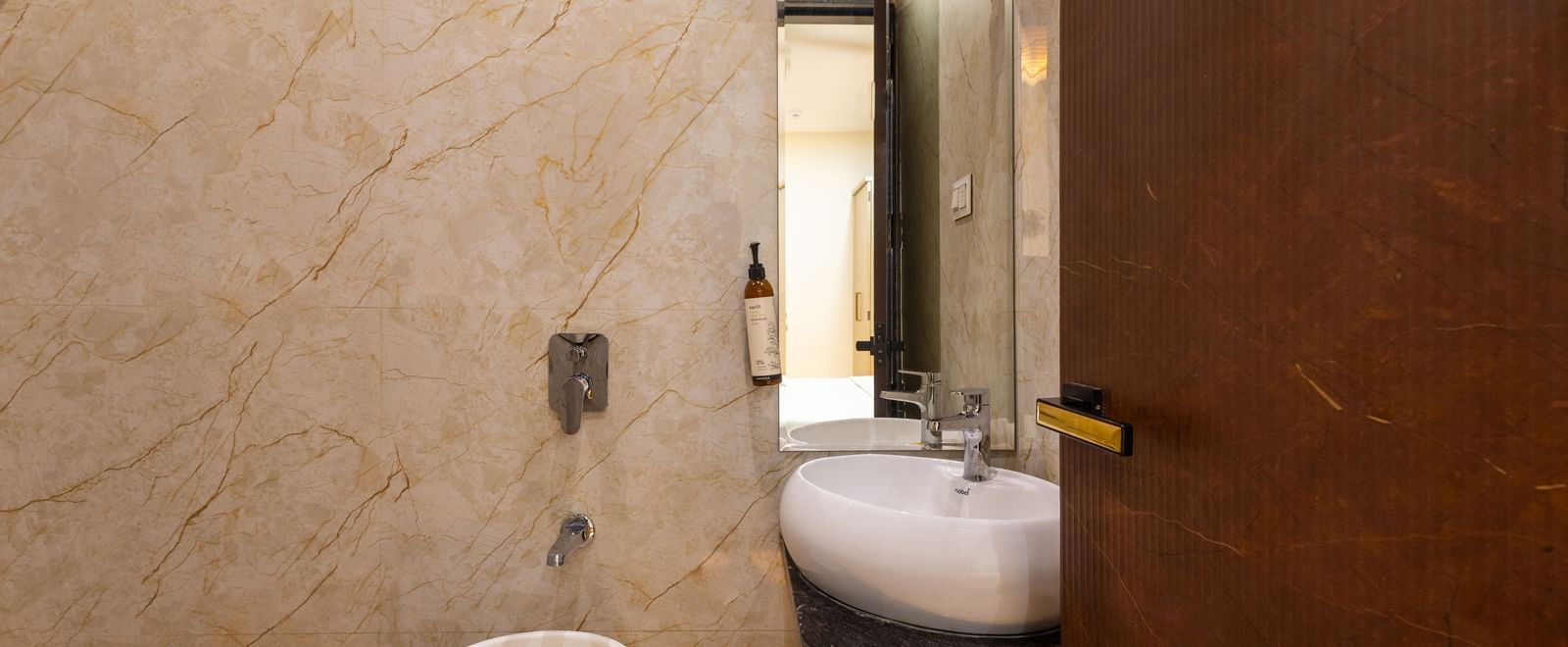 Bathroom with shower area, a mirror, and sink near a wooden door at Pravasa Stay Dewas Naka, Indore.