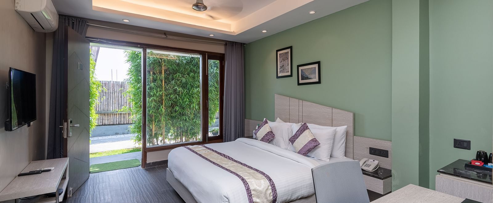 Spacious room at DLS Forest Vines Resort featuring a large bed, a bedside table, a table with chairs, and a large glass door leading to the balcony.