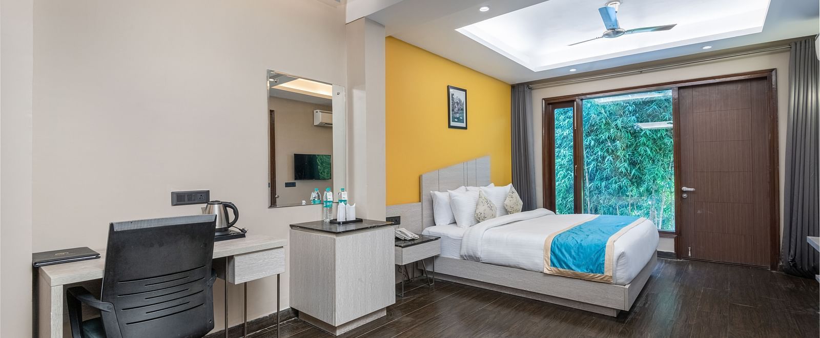 A spacious room at DLS Forest Vines Resort featuring a large bed, glass windows, a desk, and a chair.
