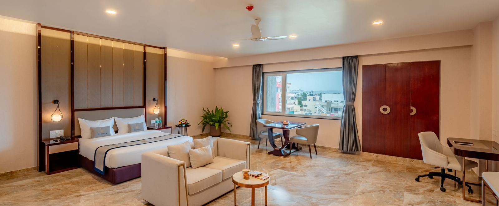 Spacious suite featuring a comfortable bed, a work desk, and city views | Suite | Pravasa Hotel, Vijayapura