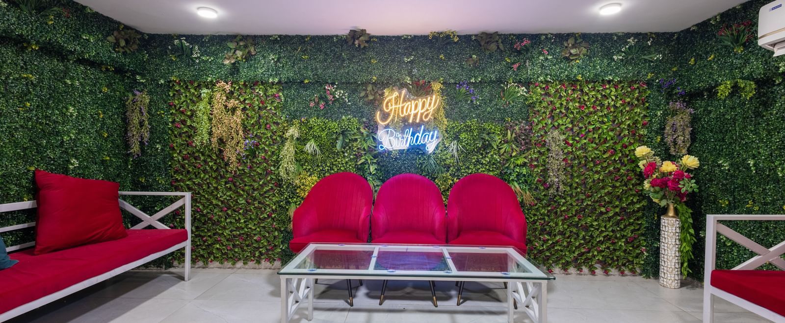 Seating lounge with red sofas, glass table, and green vertical garden wall at Pravasa Stay Dewas Naka, Indore.