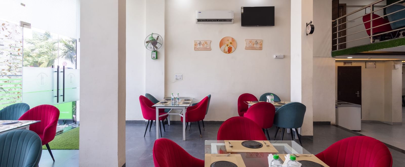 Indoor dining space with red and blue chairs around tables near glass doors at Pravasa Stay Dewas Naka, Indore.
