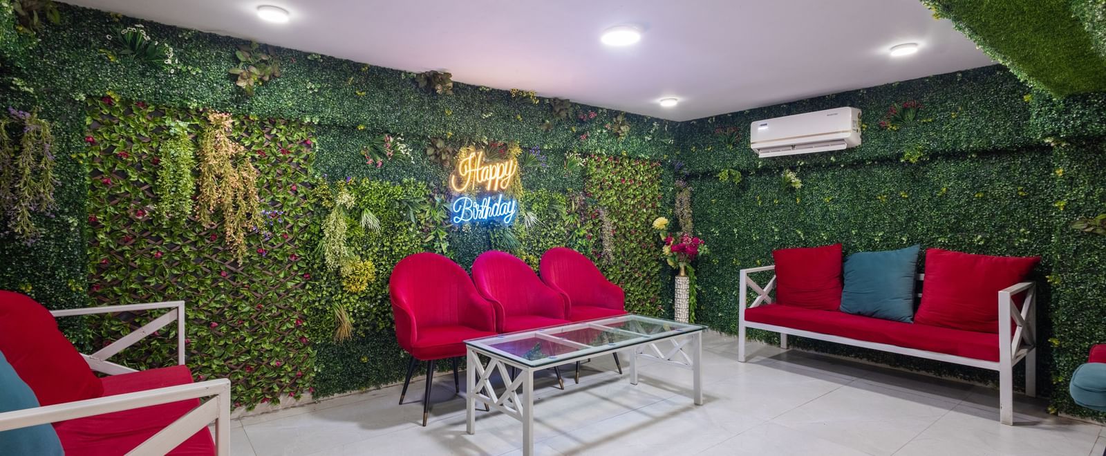 Lounge with red sofas, a glass table, and greenery-covered wall at Pravasa Stay Dewas Naka, Indore.