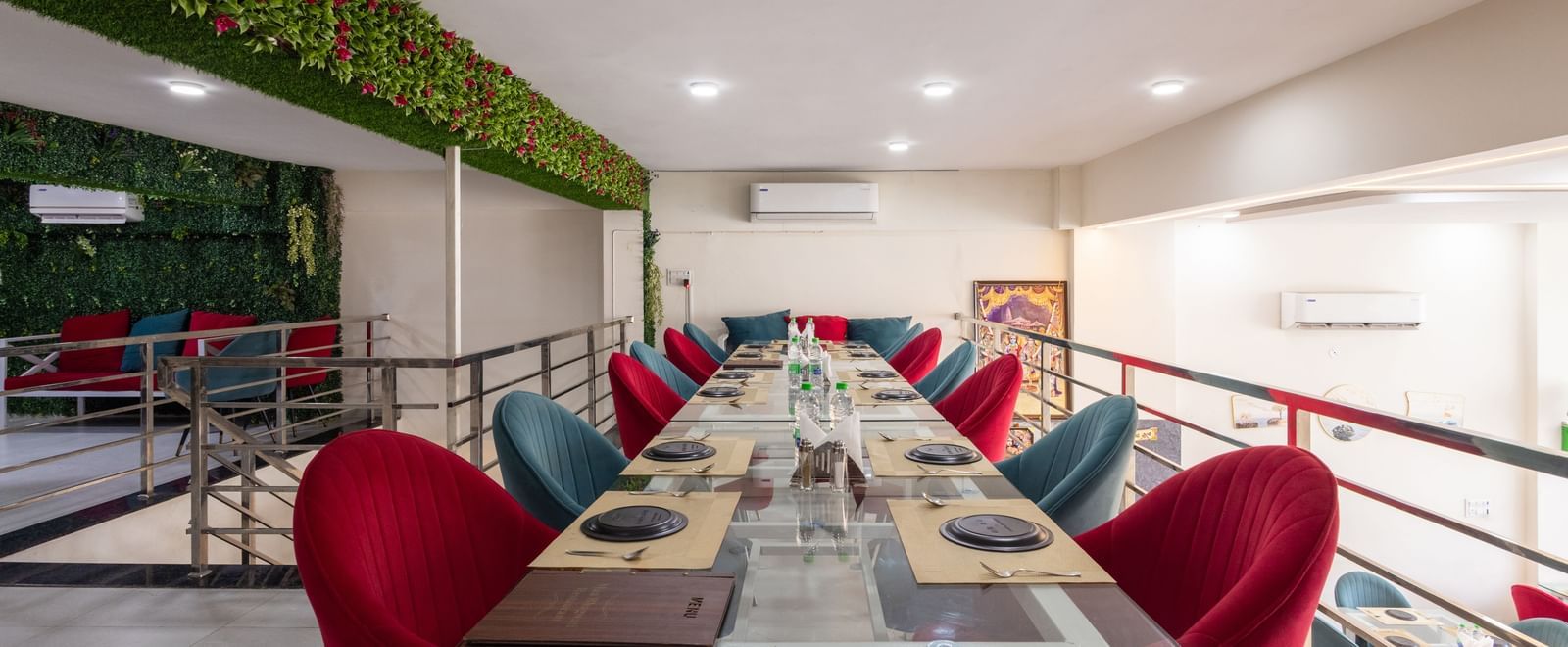 Long dining table setup with red & blue chairs and green decor on the wall at Pravasa Stay Dewas Naka, Indore.