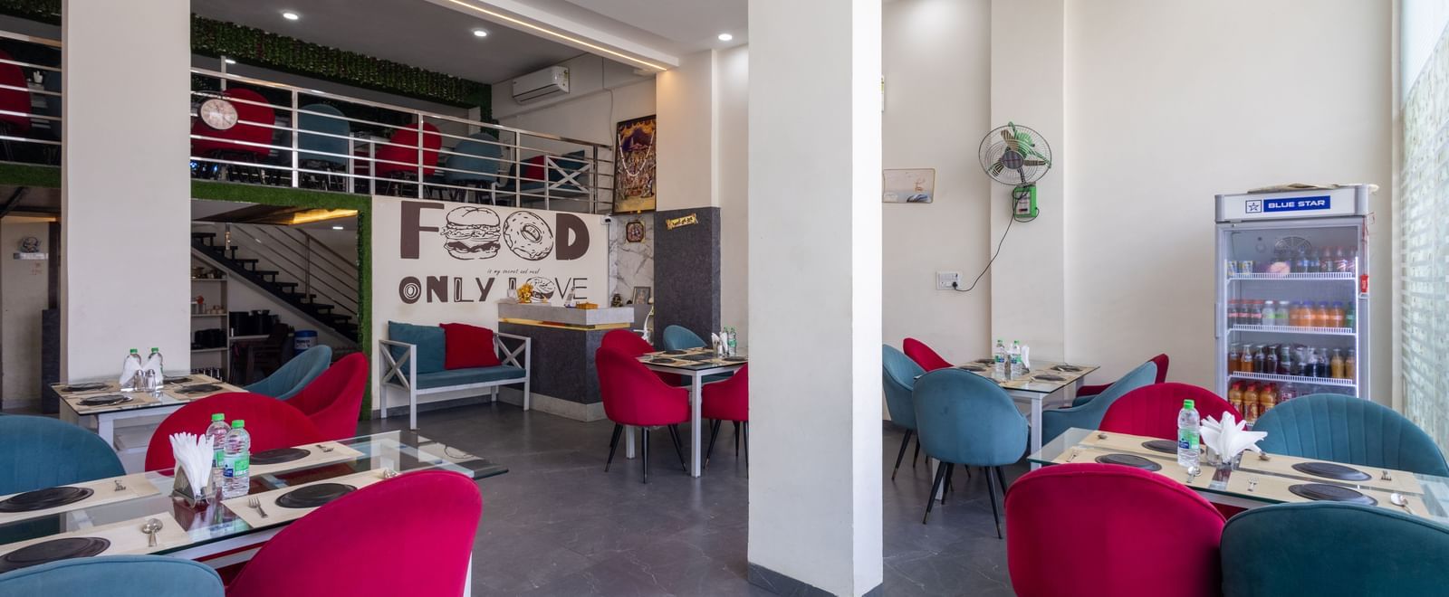 Indoor dining area with tables, red and blue chairs, and wall decor at Pravasa Stay Dewas Naka, Indore.