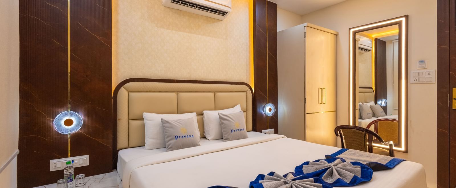 A well lit room with a double bed, side tables, mirror with a chair, and air conditioning at Pravasa Stay Dewas Naka, Indore.