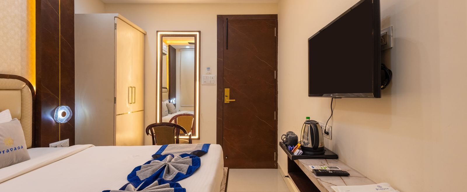 Room featuring a double bed, wall-mounted TV, a mirror with a chair, and wardrobe at Pravasa Stay Dewas Naka, Indore.