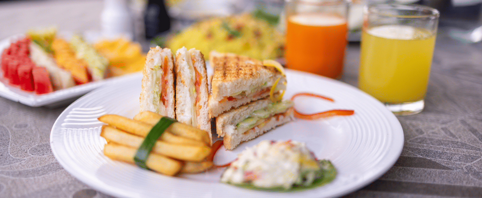 View of a cut sandwich on a plate with glasses of juice and other food at Pravasa Stay Luv Kush, Indore.
