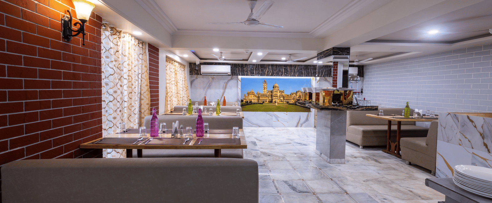 Spacious, brightly lit restaurant interior with neutral-toned seating, exposed brick wall accents, and marble flooring at Pravasa Stay, Vadodara.