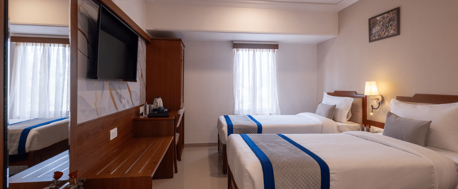 View of the twin-bedded hotel room, reflected partially in the large, dark wooden mirror over the desk/console at Pravasa Stay, Vadodara.