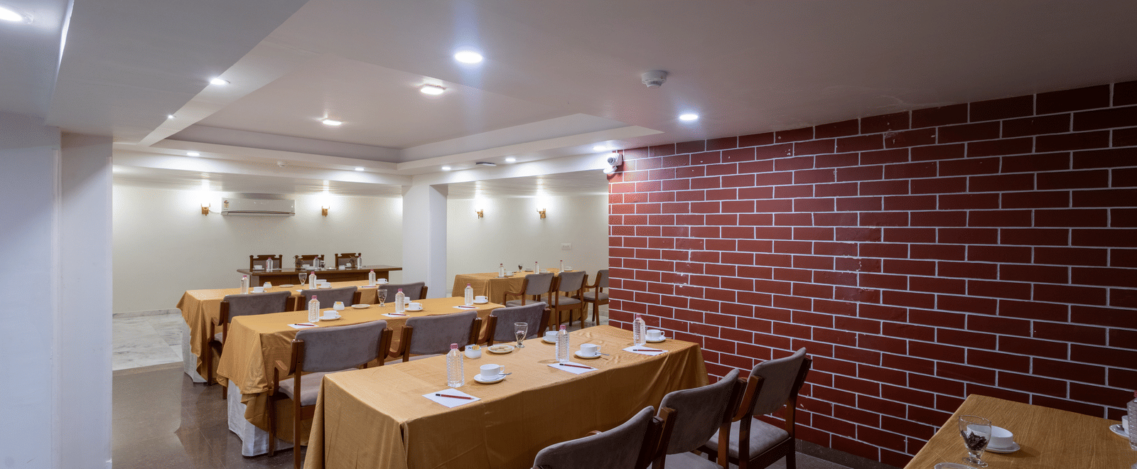 Dining space configured with long tables and chairs, covered in orange cloth, suitable for a meeting or group event at Pravasa Stay, Vadodara.