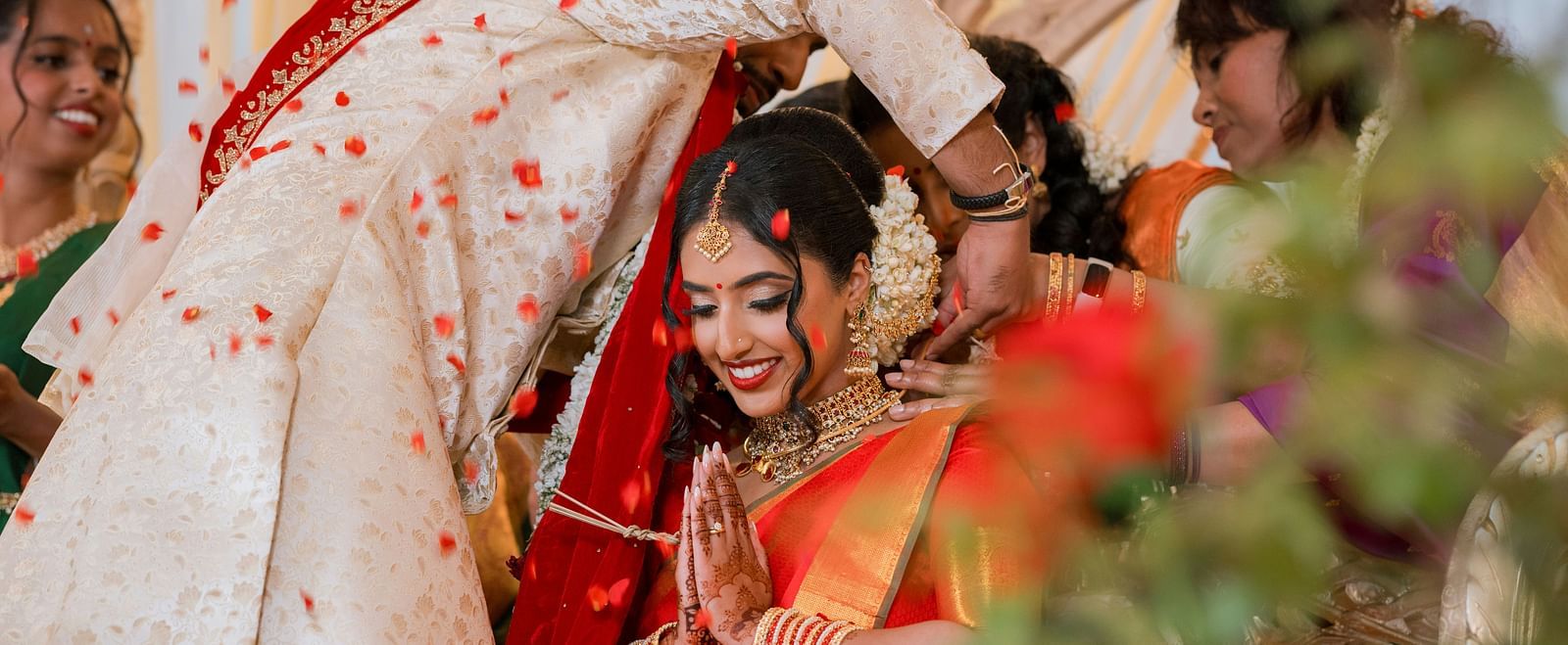 The broom tying a mangalsutra (sacred matrimonial thread) around the bride's neck as she joins her hand in prayer.