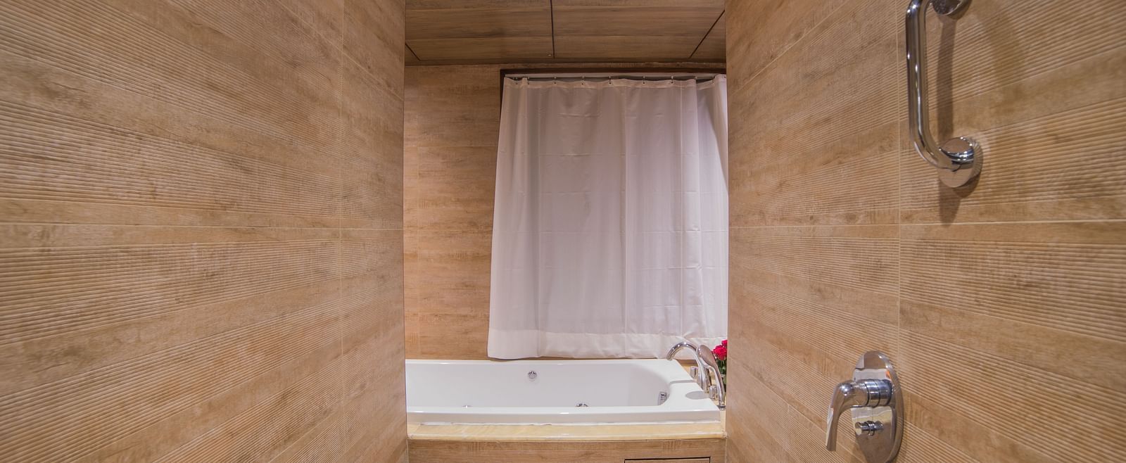 A simple hotel bathroom with a bathtub and shower combination, tiled in beige A grand hotel suite with an opulent red and white decor, large bed, and seating area, reflecting a traditional style at Sitara Luxury Hotel in Hyderabad near Ramoji Film City.