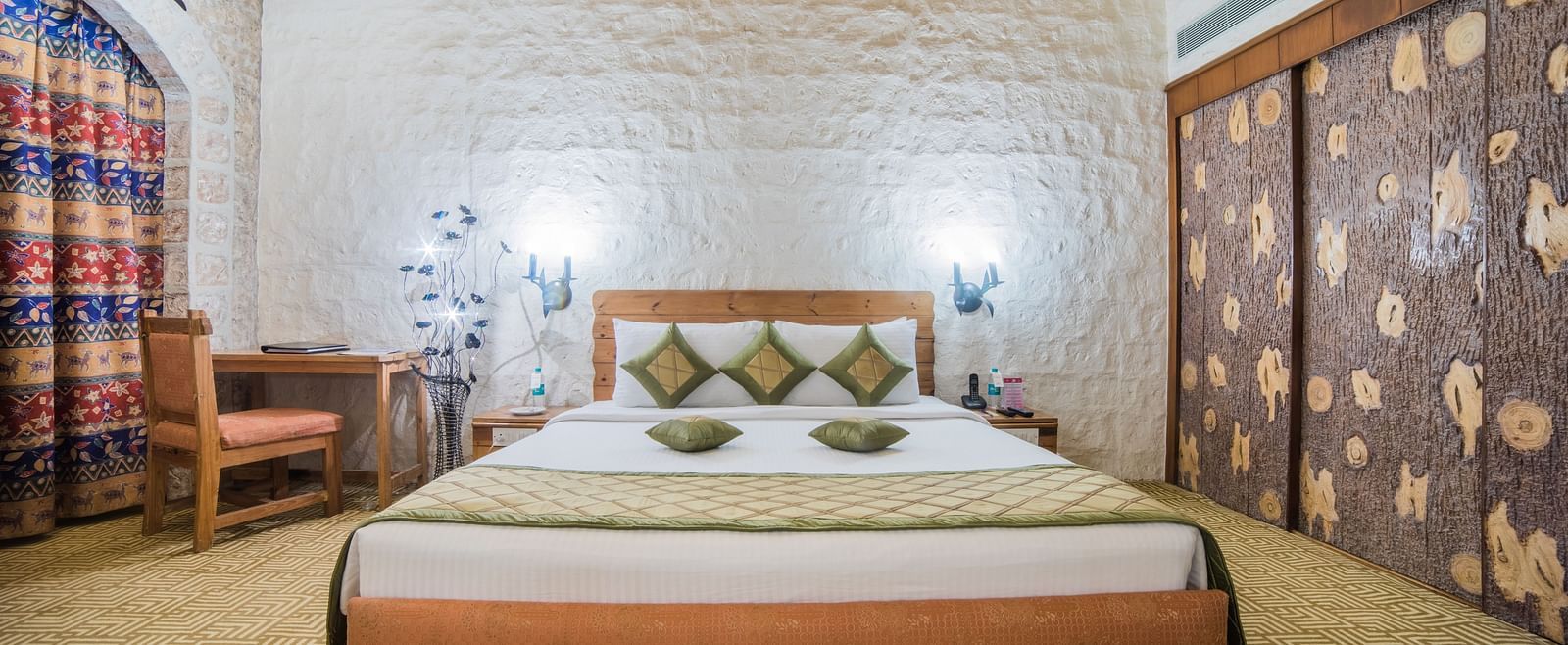 A hotel bedroom with a traditional design, featuring a large bed and stone walls adorned with textile art at Sitara Luxury Hotel in Hyderabad near Ramoji Film City.