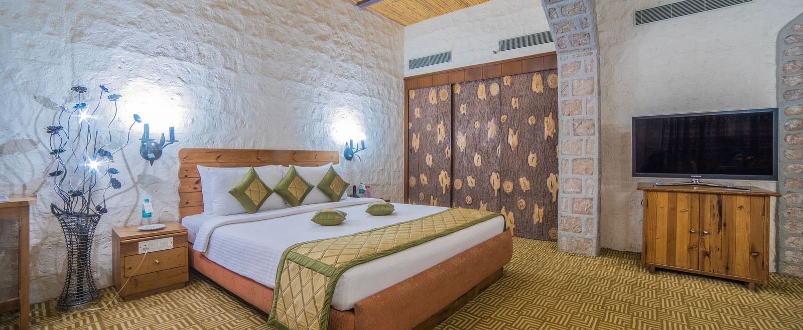 A cozy hotel bedroom with a large bed, wooden accents, and a traditional aesthetic under a vaulted ceiling at  Sitara Luxury Hotel in Hyderabad near Ramoji Film City.