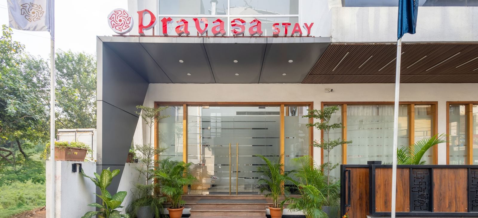 Facade and entry to Pravasa Stay Vijay Nagar, Indore, lined by potted plants on both sides, and an illuminated logo placed on the elevated ceiling.