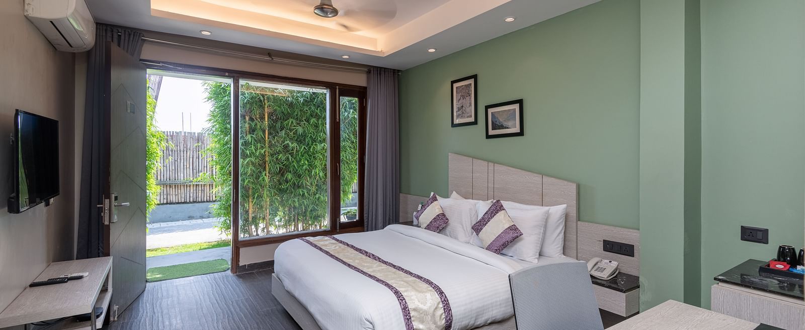 Spacious room at DLS Forest Vines Resort featuring a large bed, a bedside table, a table with chairs, and a large glass door leading to the balcony.