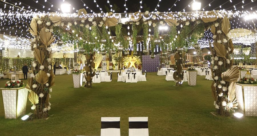 An outdoor wedding venue decorated with string lights, floral arrangements, and hanging greenery, featuring white-clothed tables and a grassy lawn at Pride Premier Dehradun
