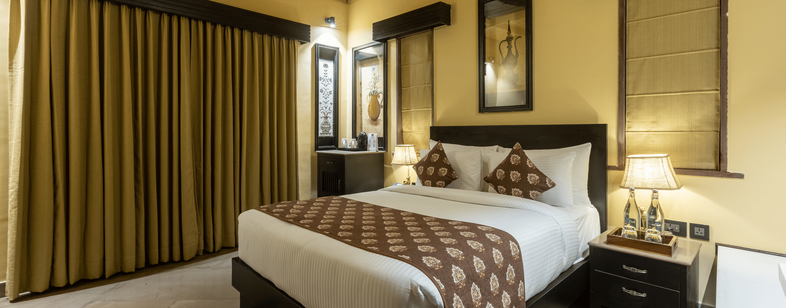 A cosy bedroom at Aamaghati Wildlife Resort with a king size bed, soft lighting, and large windows offering a serene stay.