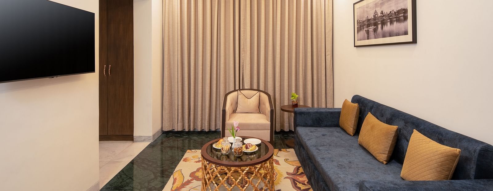An image of a seating area with sofa set, centre table, flat TV screen and a photo frame hanged on the wall -  Brij Eternity, Vrindavan