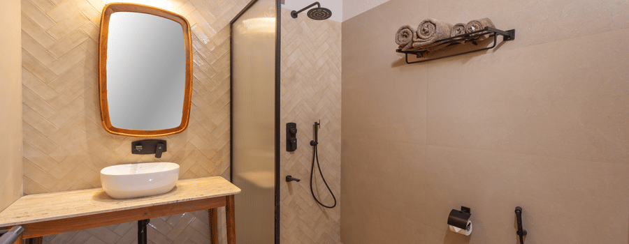 A bathroom showing a wooden vanity unit with a white basin and mirror, next to a glass-partitioned shower area | Samsara Hill Resort, Mussoorie