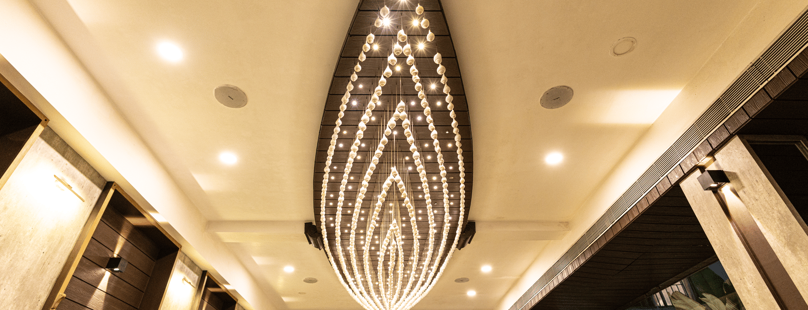 The ceiling view of the dining area at Hotel Seagull Digha showing a long decorative chandelier, lighting, and corridor walls on both sides.
