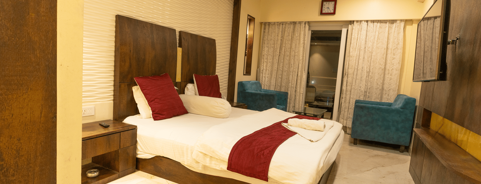 A bedroom with a king size bed, red cushions, a rug, 2 armchairs and a side table at Hotel Seagull Digha.