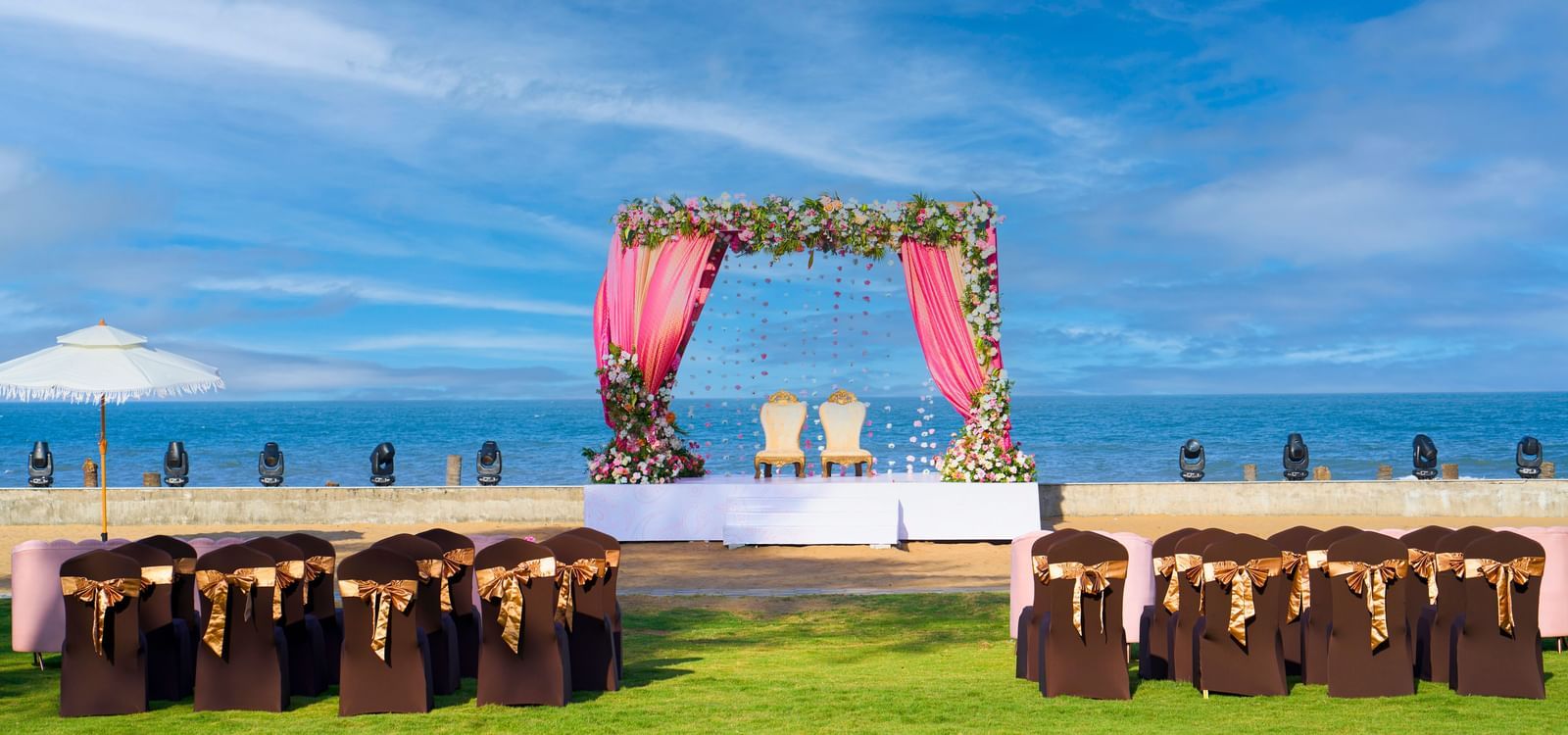Outdoor lawn with decorated chairs, platform stage decorated with flowers & the view of the blue sky & sea at Grande Bay Resort & Spa.