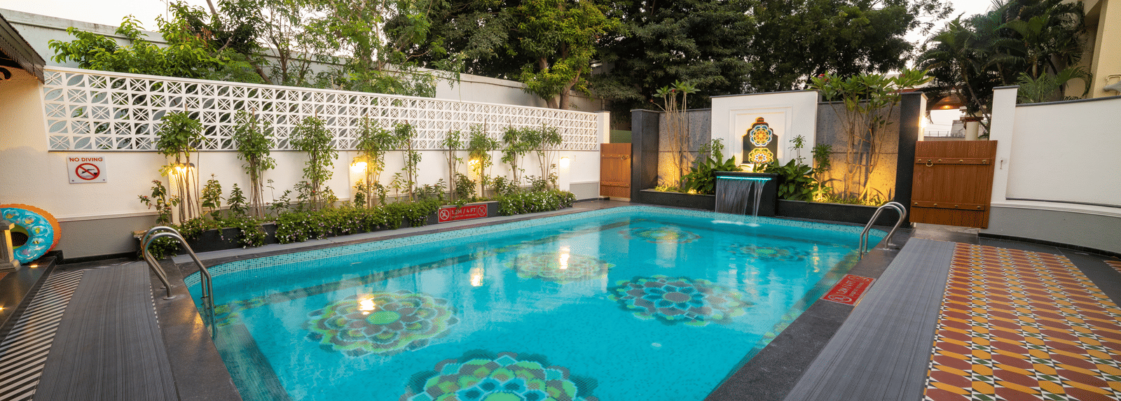 Beautifully lit poolside seating under a red canopy at night. Regency Madurai by GRT Hotels
