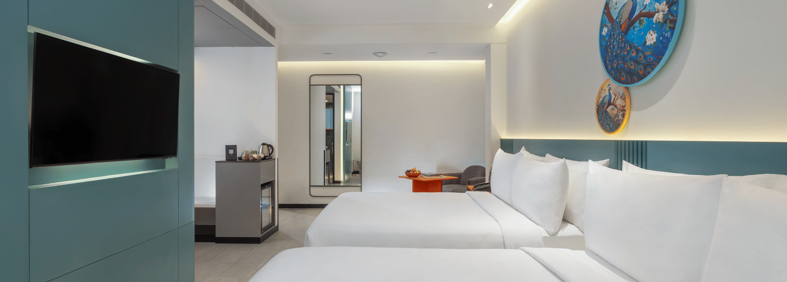 A hotel room featuring two large beds, a wall-mounted television, a ceiling fan, and a minibar at Zibe Luxe | Best Hotels to stay in hyderabad