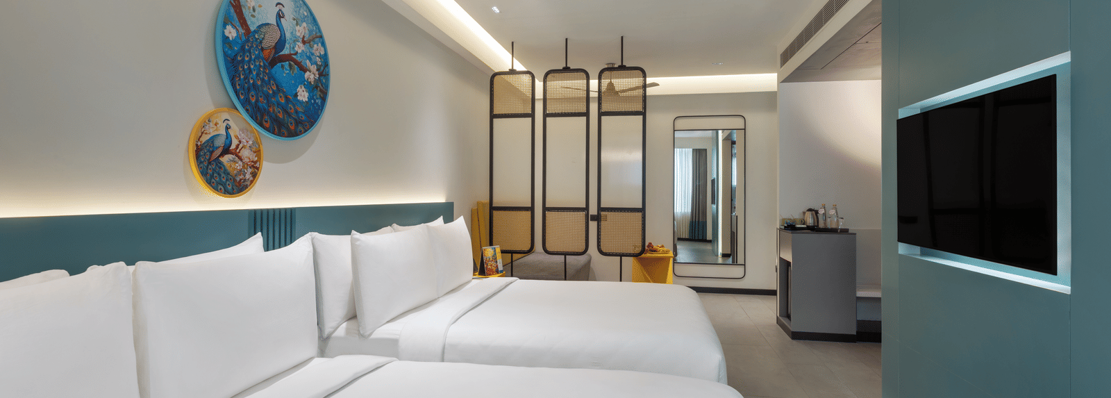 A hotel room with 2 large beds, a wall-mounted TV, a ceiling fan, and a separate seating area making it the best place to stay in Hyderabad for business stays | Zibe Luxe Hyderabad by GRT Hotels