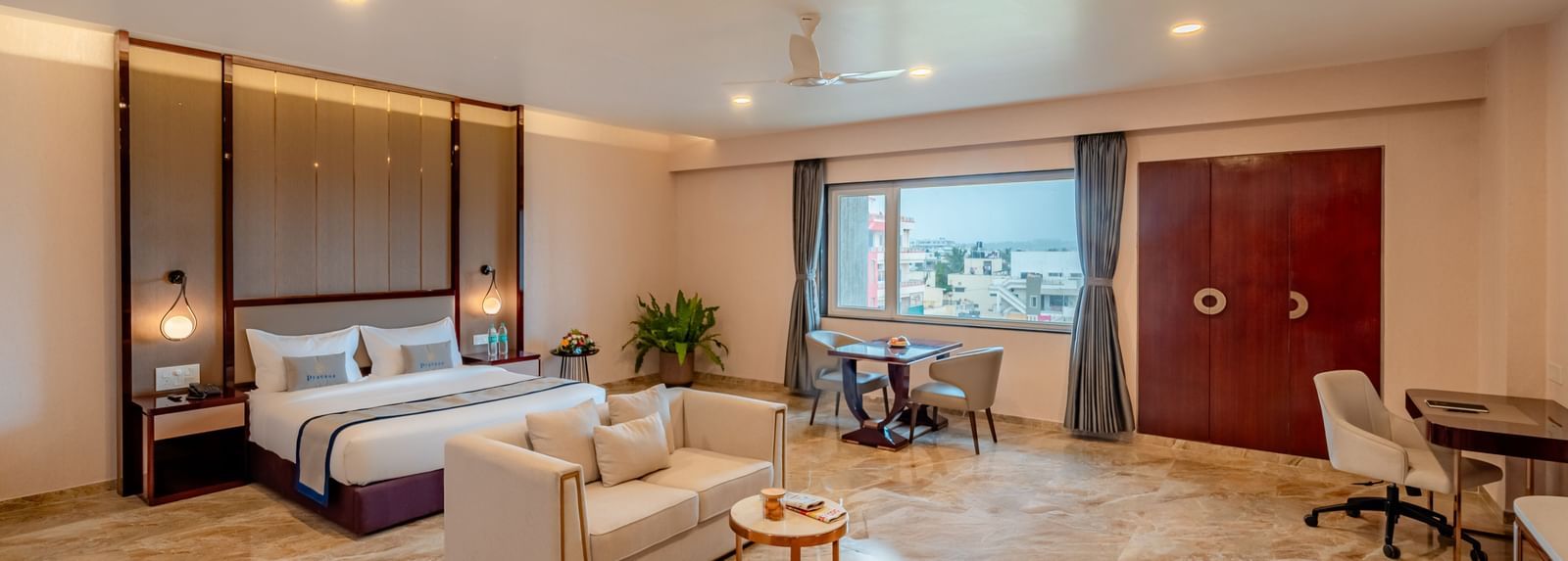 Spacious suite featuring a comfortable bed, a work desk, and city views | Suite | Pravasa Hotel, Vijayapura