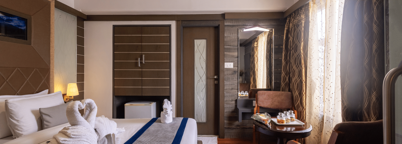 View of the bed reflected in a large mirror/television screen, highlighting the room's warm tones and wooden features at Pravasa Stay, Vadodara.