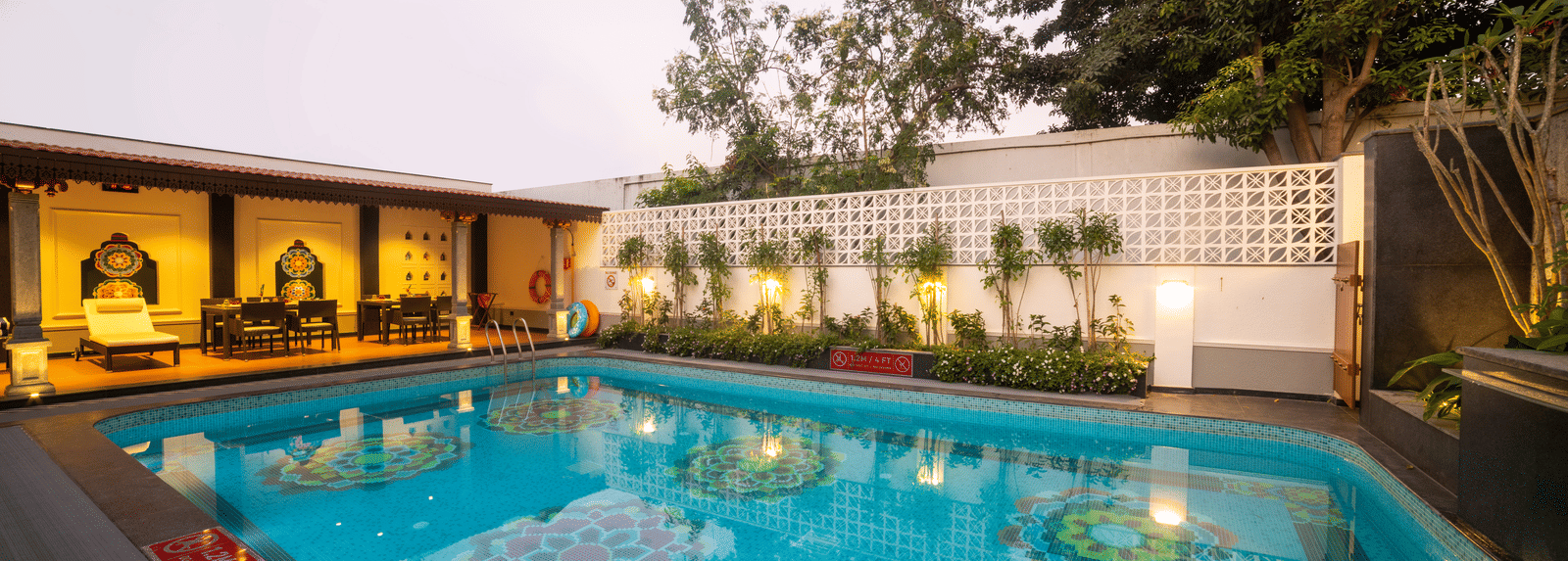 Bright blue pool surrounded by greenery and elegant deck seating. Regency Madurai by GRT Hotels