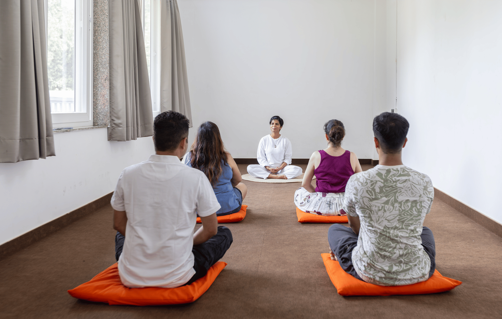 A group of 5 people sitting on mats for meditation indoors at Megha Resort & Villas, Dehradun.