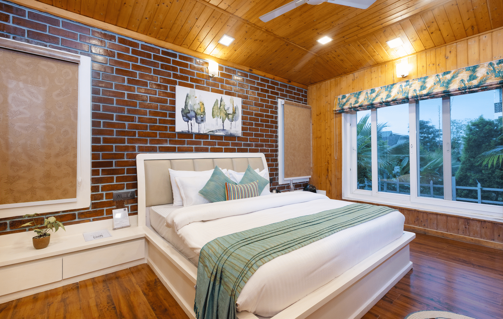 A bright, rustic bedroom with a king sized bed, wooden walls, and a large window with a view - Megha Resort & Villas, Dehradun