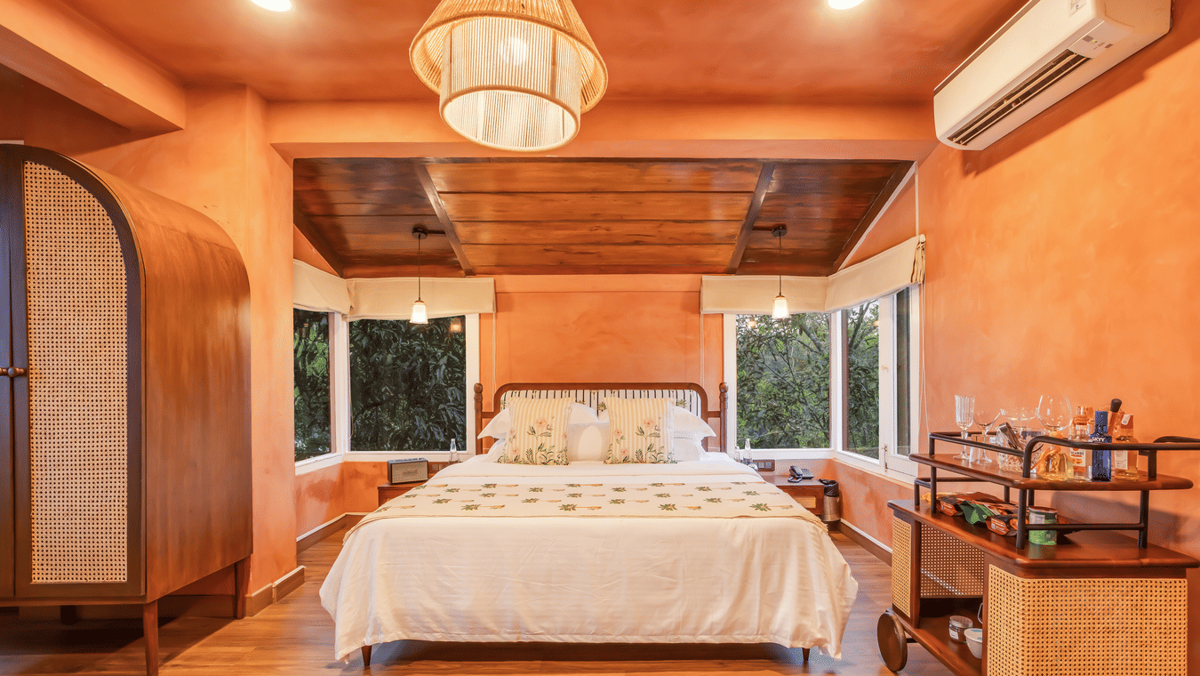 View of the Penthouse at Unseen Boutique Hotel Assagao Goa with a king bed, rattan pendant light, wooden ceiling, and warm natural light.