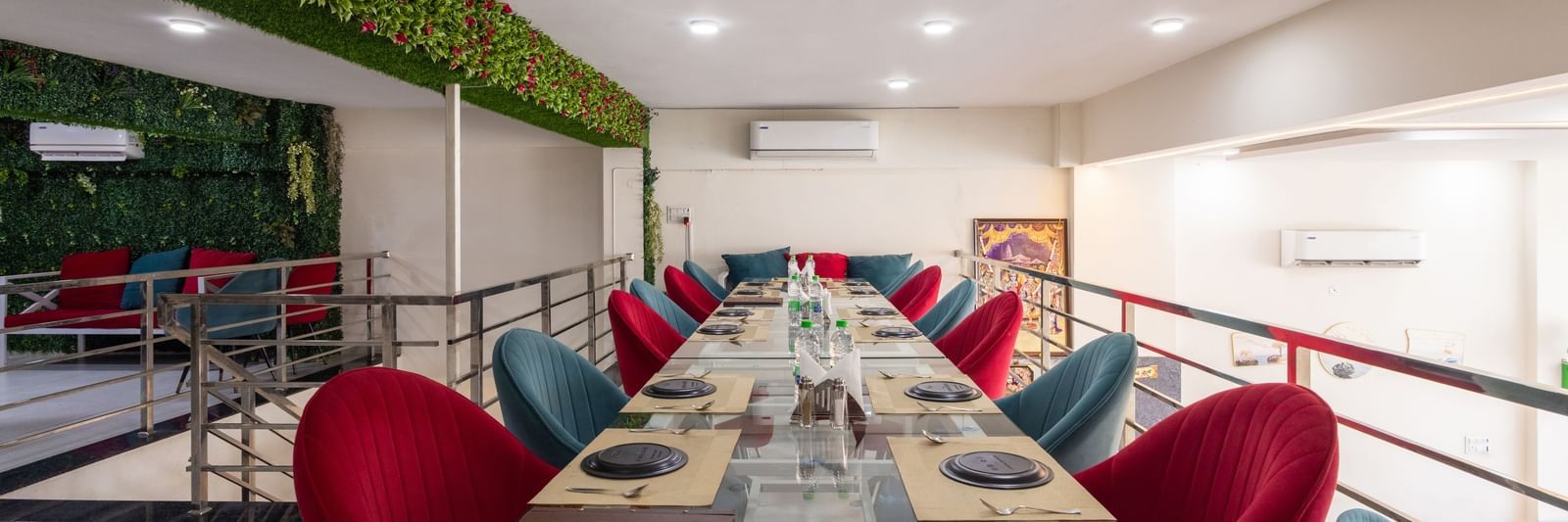 Long dining table setup with red & blue chairs and green decor on the wall at Pravasa Stay Dewas Naka, Indore.