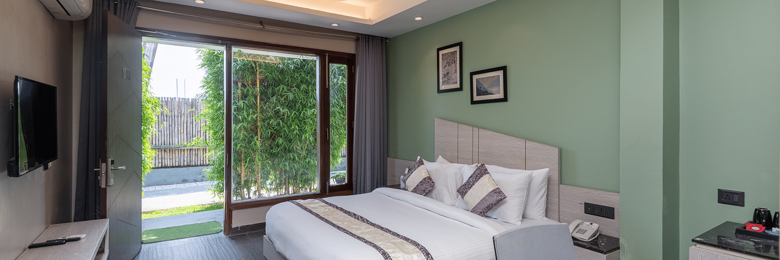 Spacious room at DLS Forest Vines Resort featuring a large bed, a bedside table, a table with chairs, and a large glass door leading to the balcony.