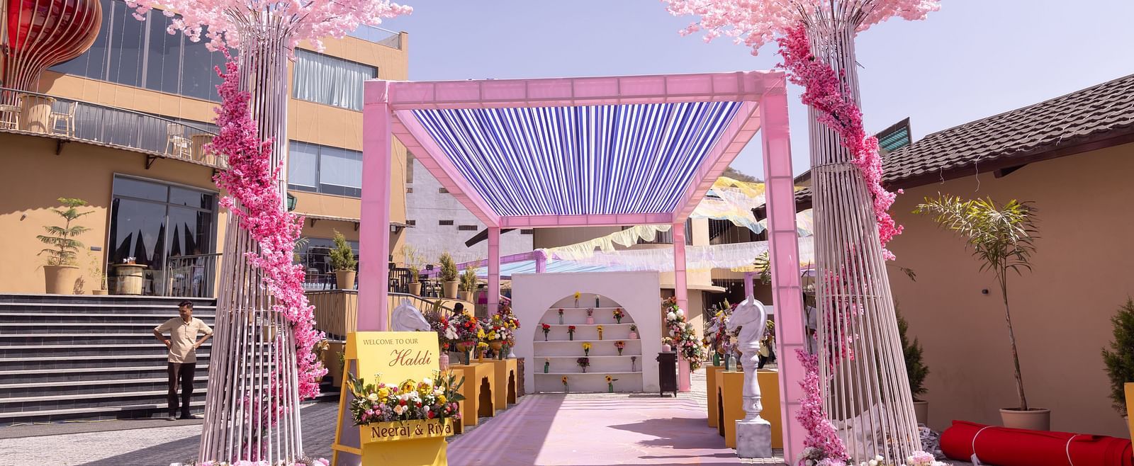 A wedding venue is decorated with pink floral arrangements and draped fabrics  | The Qualia Resort Club & Brewery, Udaipur