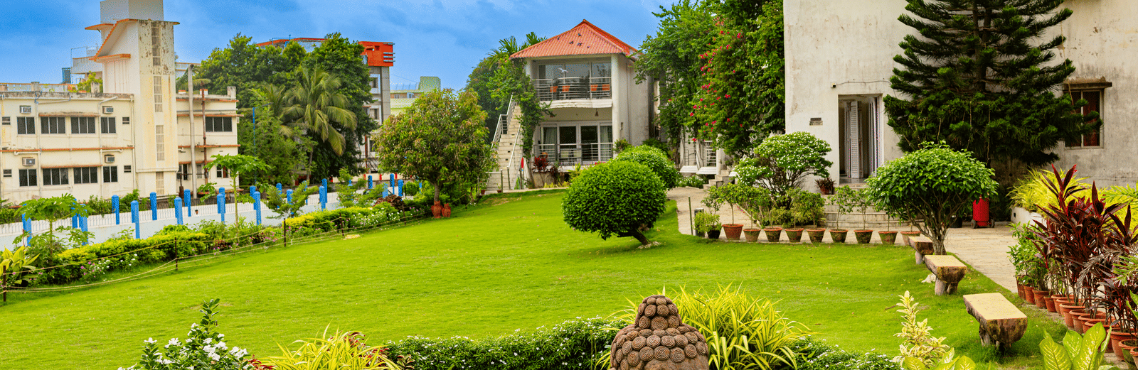 Large white resort buildings with a spacious, manicured green lawn, garden area, and trees - Hotel Seagull Digha