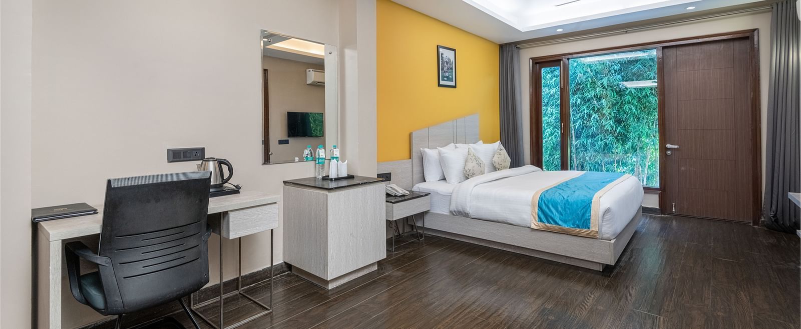 A spacious room at DLS Forest Vines Resort featuring a large bed, glass windows, a desk, and a chair.