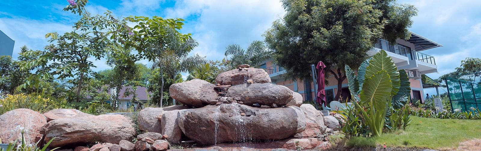 Rock waterfall feature surrounded by landscaped greenery at Trishvam Symphony, Krishnagiri.