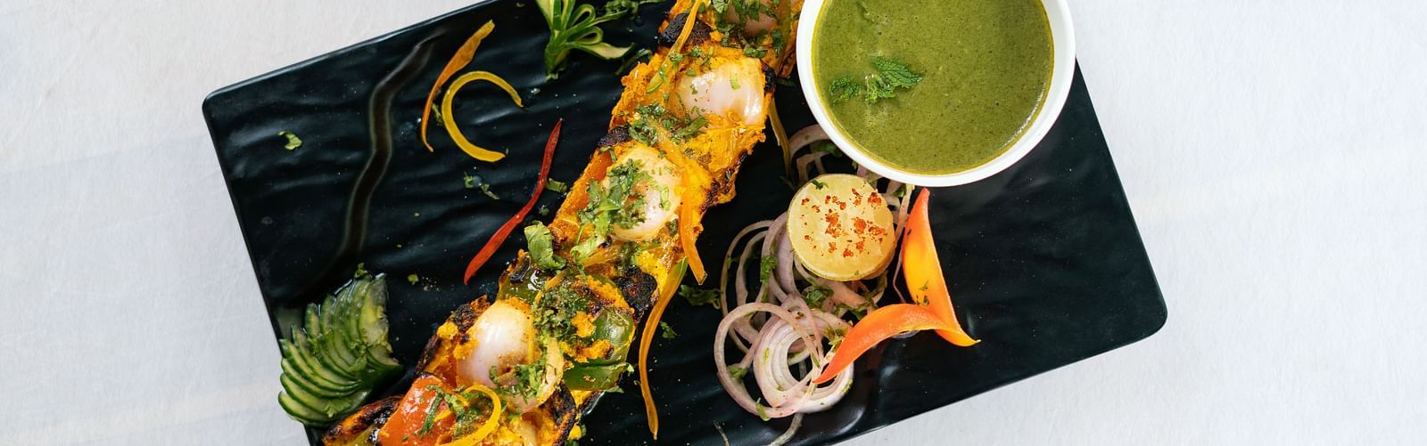 image of a paneer tikka platter served on a black rectangular dish with coriander chutney