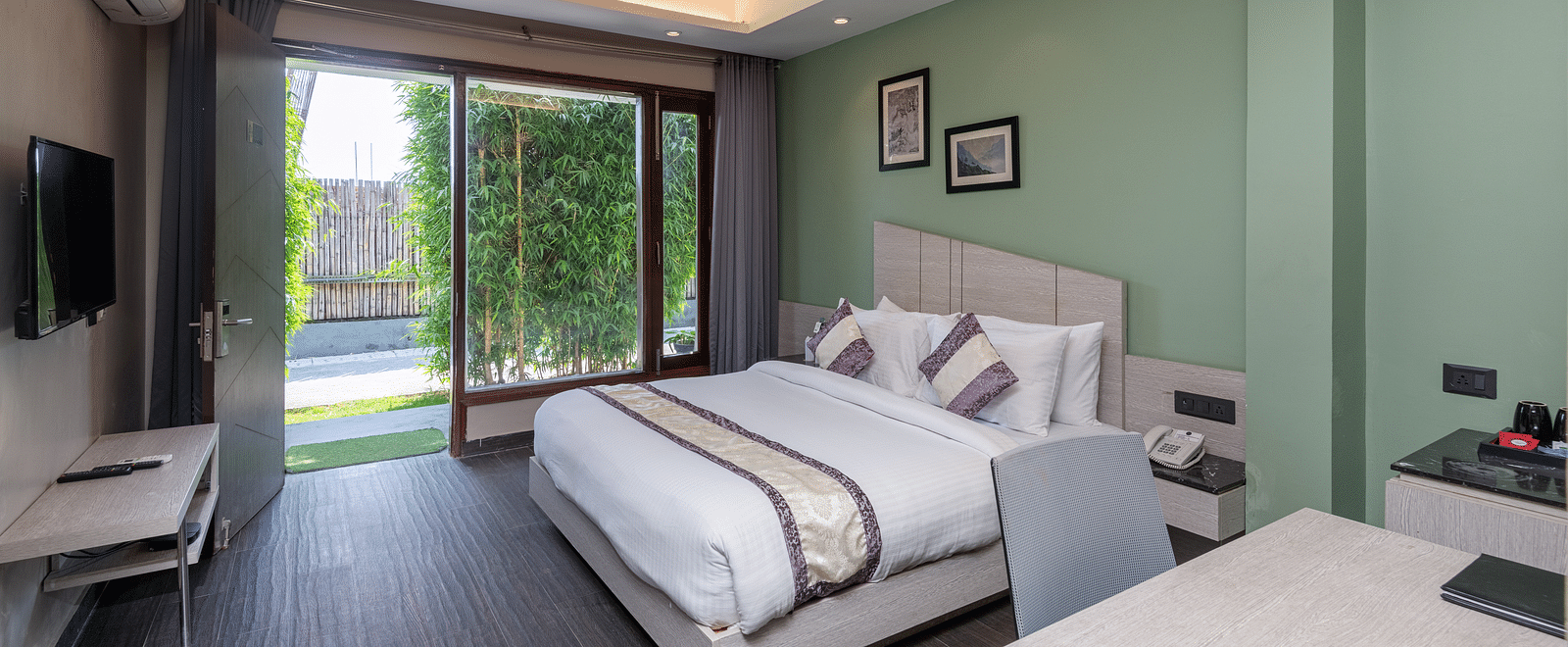 Spacious room at DLS Forest Vines Resort featuring a large bed, a bedside table, a table with chairs, and a large glass door leading to the balcony.